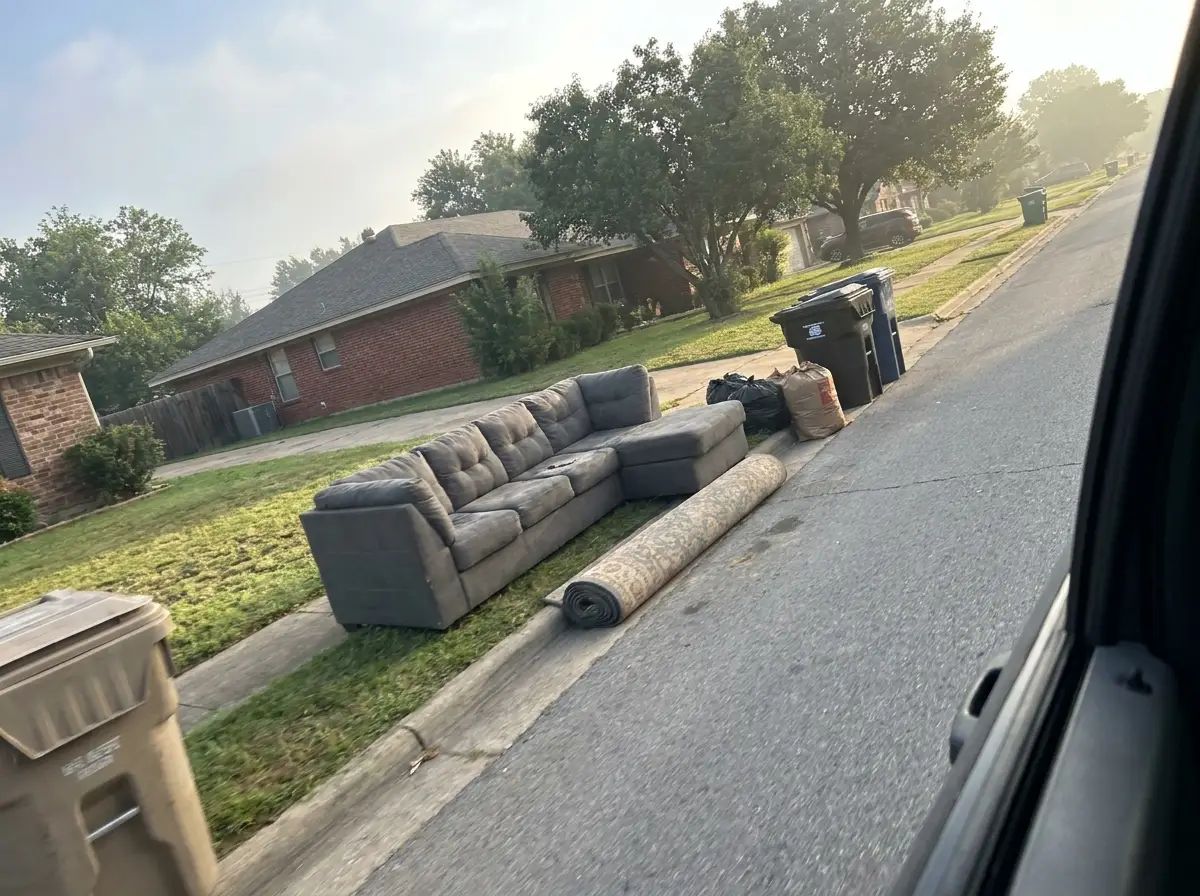 Old sectional couch and rolled rug at the curb of a suburban Katy street awaiting pickup
